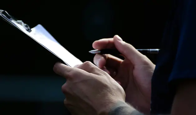 Person holding a pen writing on a clipboard